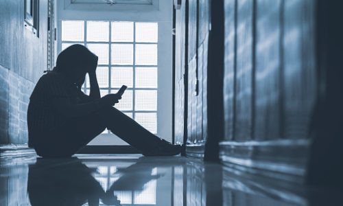 Depressed woman sitting alone and looking smartphone with holding her head on corridor in front of room at apartment in low key style