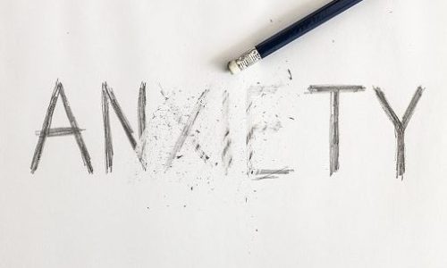 Erasing anxiety. Anxiety written on white paper with a pencil, partially erased with an eraser. Symbolic for overcoming anxiety or treating anxiety.